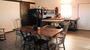Un comedor con una mesa y sillas de madera, un refrigerador negro, y una zona de cocina con armarios y un ventanal.