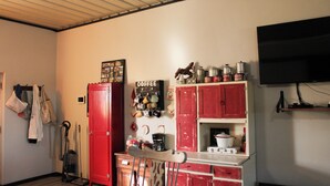Una cocina compacta con armarios rojos, una estación de café y un televisor fijado a la pared.
