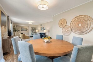 A dining room with a round wooden table, six chairs, and a fruit bowl.