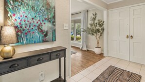 A hallway with a painting, a lamp, a potted plant, and a door.