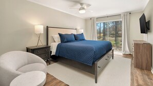 A bedroom with a bed, nightstands, a chair, a TV, and a view through a window.