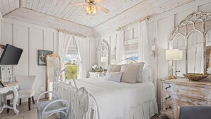 A bedroom with a bed, a vanity with a mirror, a chair, a dresser, and a television. - Romantic Dragonfly Cottage with Deeded Beach Access! Meticulously Maintained! (Orange Beach)
