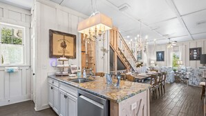 A spacious kitchen with a granite countertop, stainless steel appliances, and a wooden island. There is a dining area with a chandelier and a staircase leading to another level. - Romantic Dragonfly Cottage with Deeded Beach Access! Meticulously Maintained! (Orange Beach)