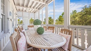 A covered outdoor patio with a wooden table and chairs, surrounded by white railings and large windows. - Romantic Dragonfly Cottage with Deeded Beach Access! Meticulously Maintained! (Orange Beach)