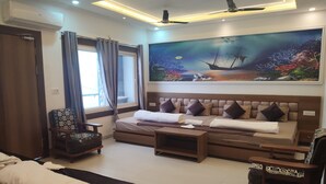 A modern hotel room with a large bed, a sofa, a wooden coffee table, and a painting of an underwater scene. - Shri Ramya Dham (Mathura)