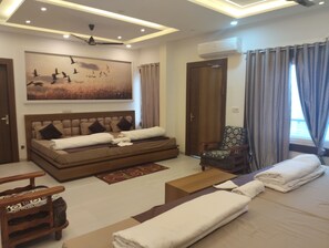 A modern hotel room with a large bed, a sofa, a wooden chair, and a ceiling fan.