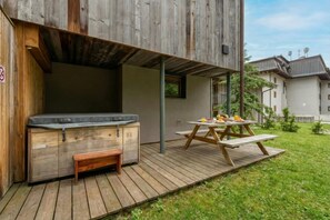 Eine Holzterrasse mit Whirlpool, einem Picknicktisch mit Essen und Blick auf benachbarte Gebäude.