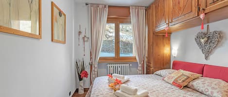 A bedroom with a bed, wooden cabinets, a window with curtains, and wall art.