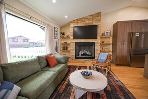 A living room with a sofa, a fireplace, a television, and a kitchen area. - Old Town | Pickleball • Pool • Spa • Putt • Firepit | Sleeps 16 (Scottsdale)