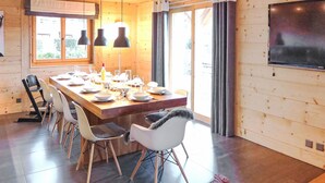 A modern dining area with a wooden table set for six, surrounded by white chairs with black cushions.