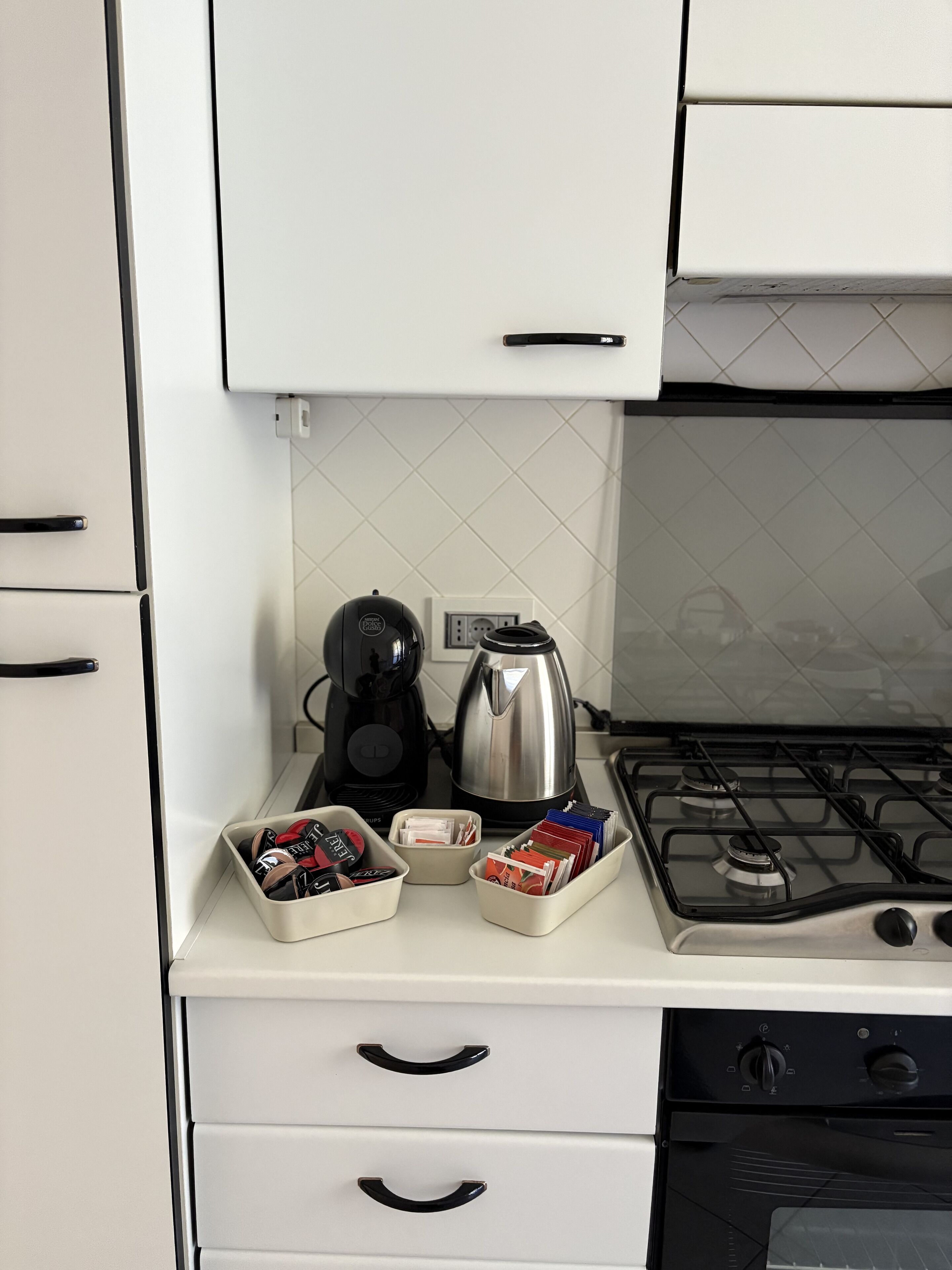A kitchen with white cabinets, a coffee maker, a kettle, and a gas stove.