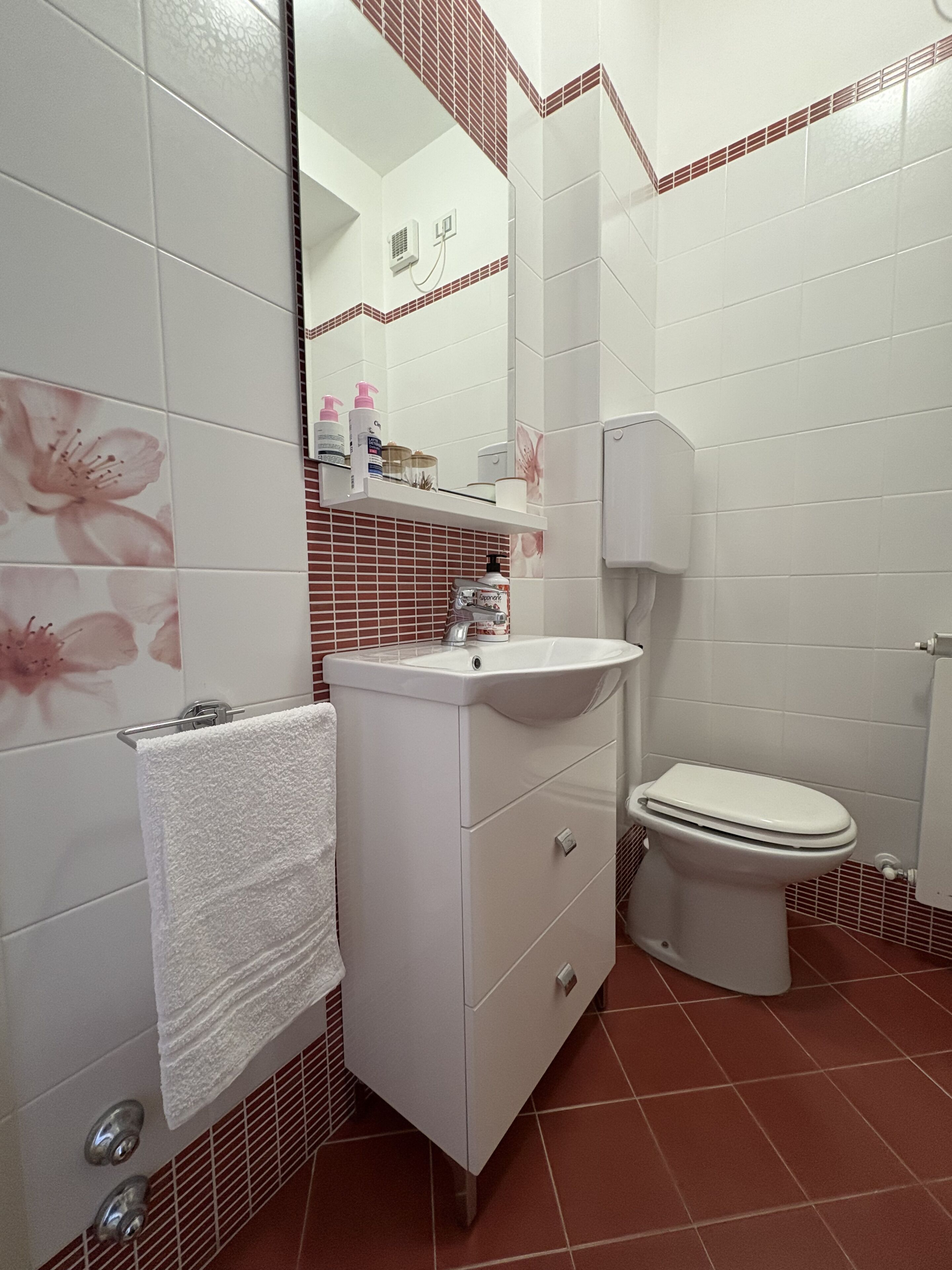 A bathroom with white tiles, a white sink, a toilet, and a mirror.
