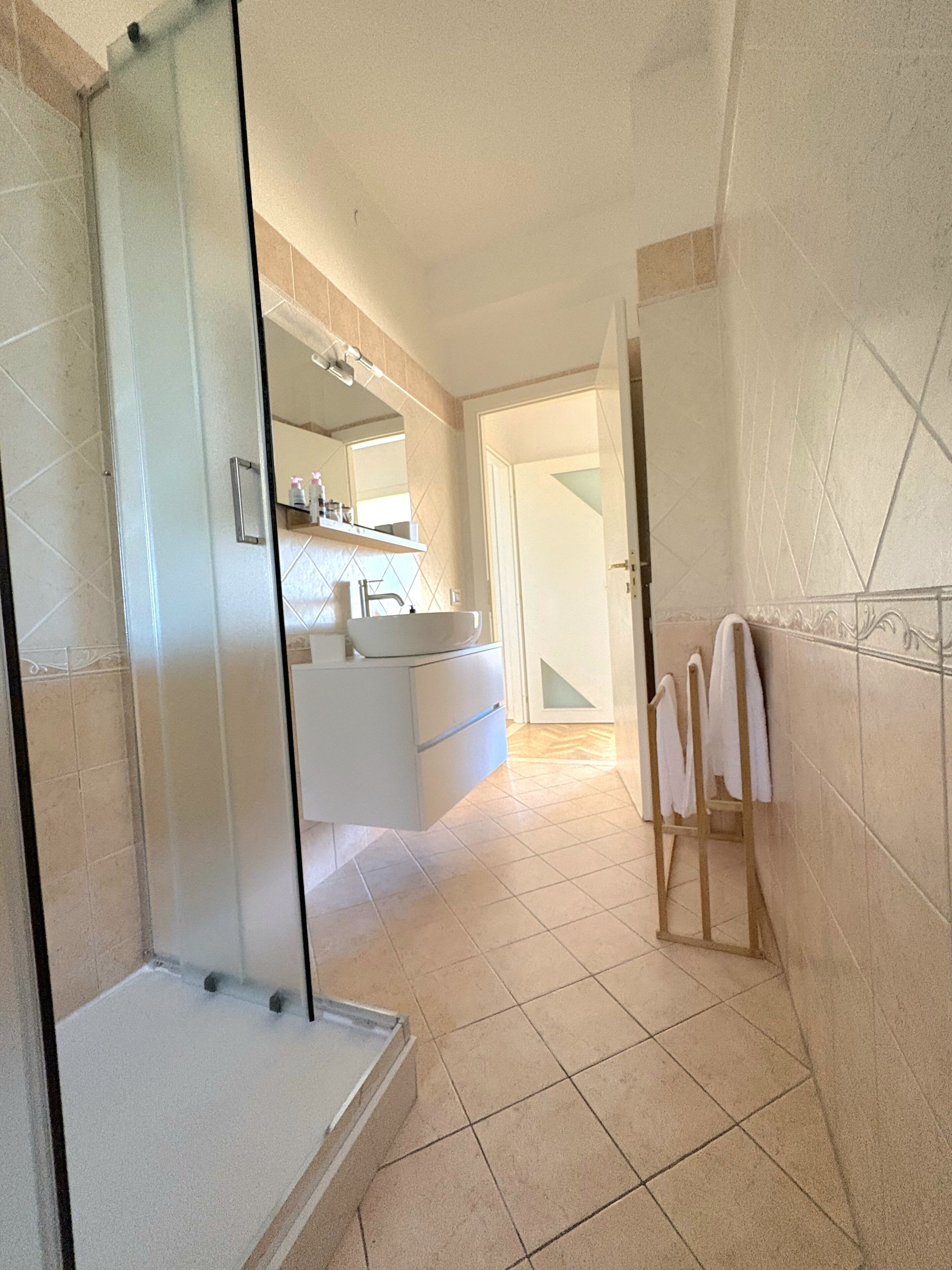 A bathroom with a glass shower enclosure, a white sink, and a mirror above it.