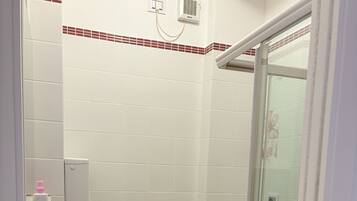 A bathroom with white tiles, a glass shower enclosure, a white sink, and two toilets.