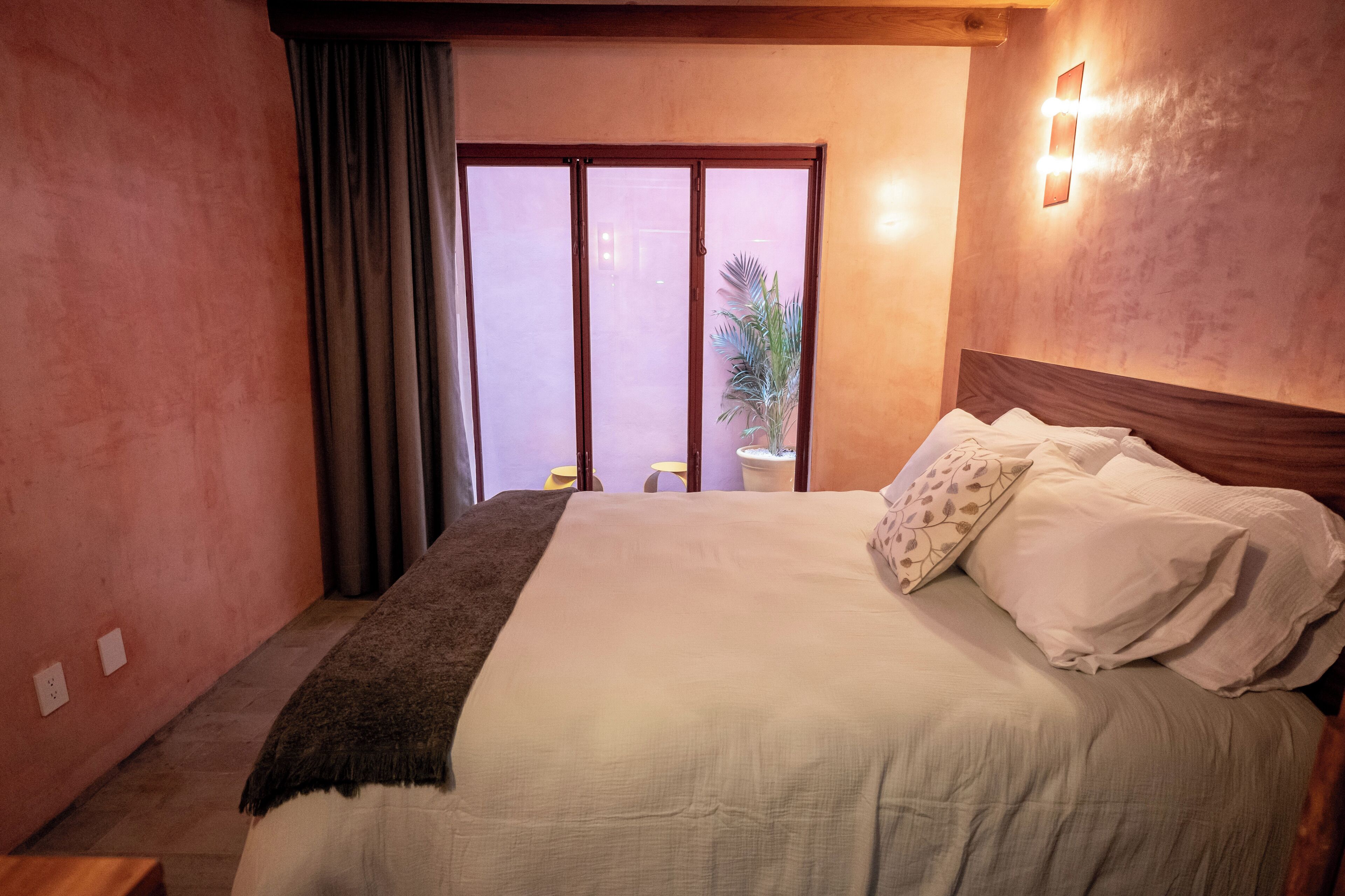 A bedroom with a large bed, a wooden headboard, a sliding glass door, and a small bedside table with a lamp.