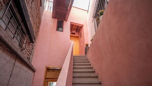 A narrow stairway leading to a wooden door, flanked by pink walls and a window with a metal grille. - Hotel Casa de las Abuelas (Guanajuato)