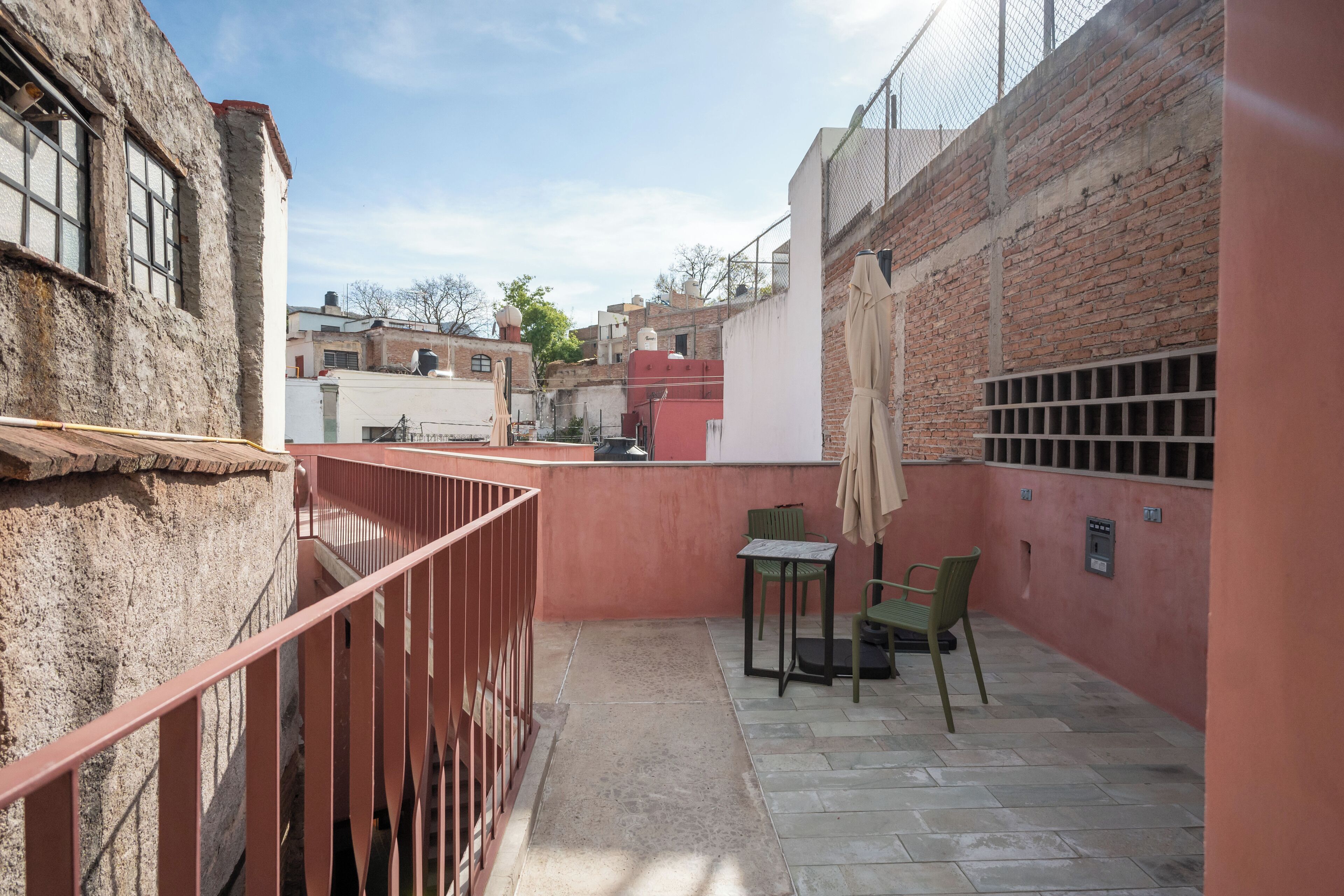 Une ruelle étroite avec un petit patio comprenant une table et des chaises, une rambarde en métal et un mur de briques.