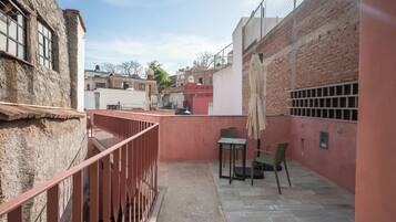 Une ruelle étroite avec un petit patio comprenant une table et des chaises, une rambarde en métal et un mur de briques.