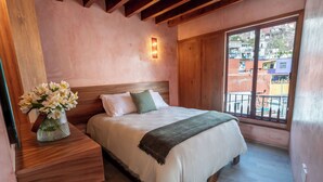 A bedroom with a wooden headboard, a large window with a balcony, and a bedside table with a vase of flowers. - Hotel Casa de las Abuelas (Guanajuato)