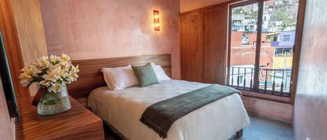 A bedroom with a wooden headboard, a large window with a balcony, and a bedside table with a vase of flowers.