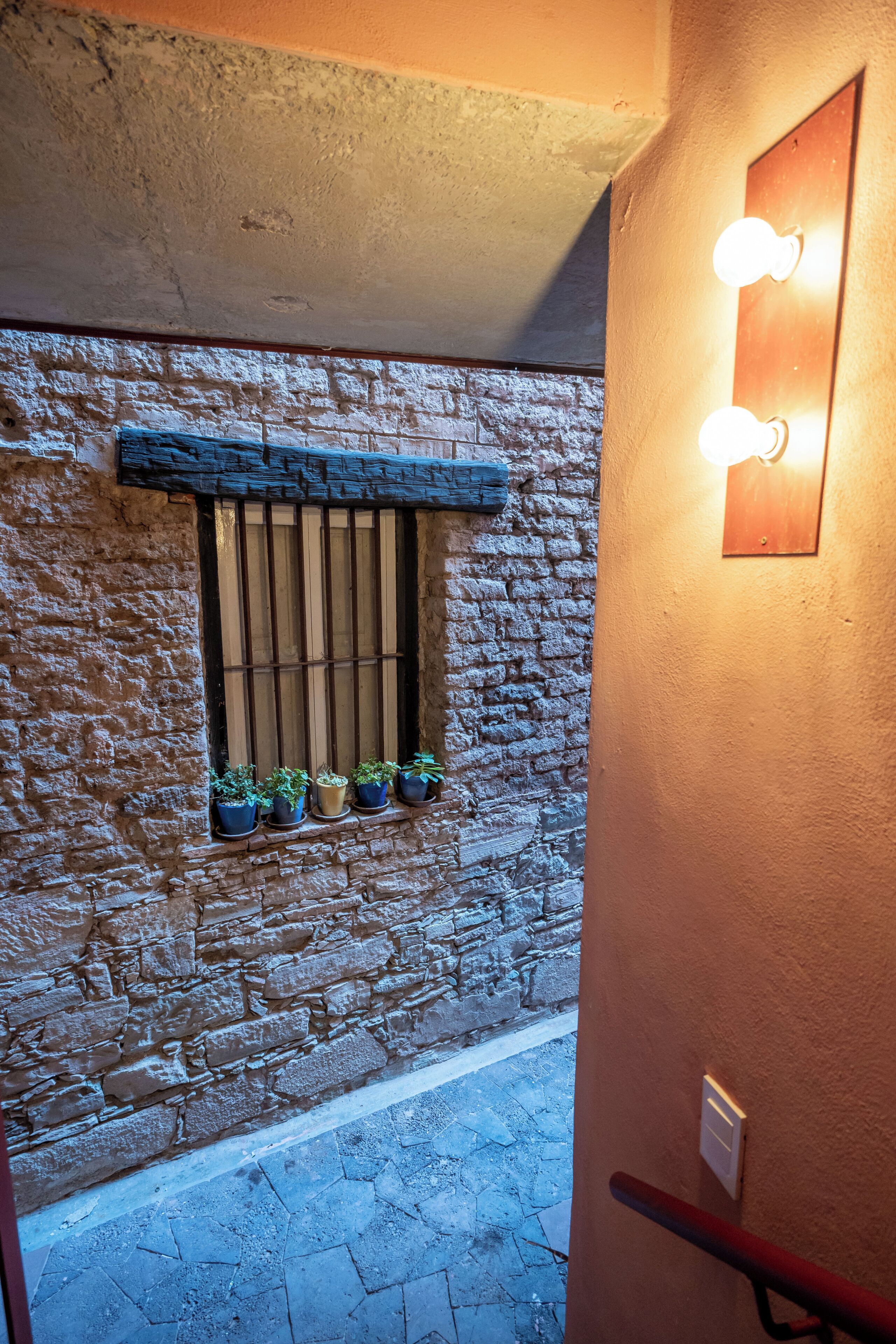 A stone wall with a window and potted plants, a wooden beam above the window, and a wall-mounted light fixture.
