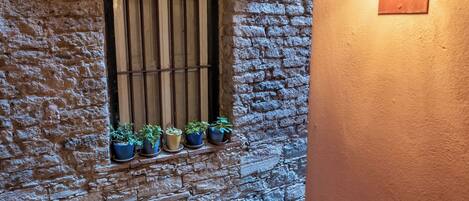 A stone wall with a window and potted plants, a wooden beam above the window, and a wall-mounted light fixture.