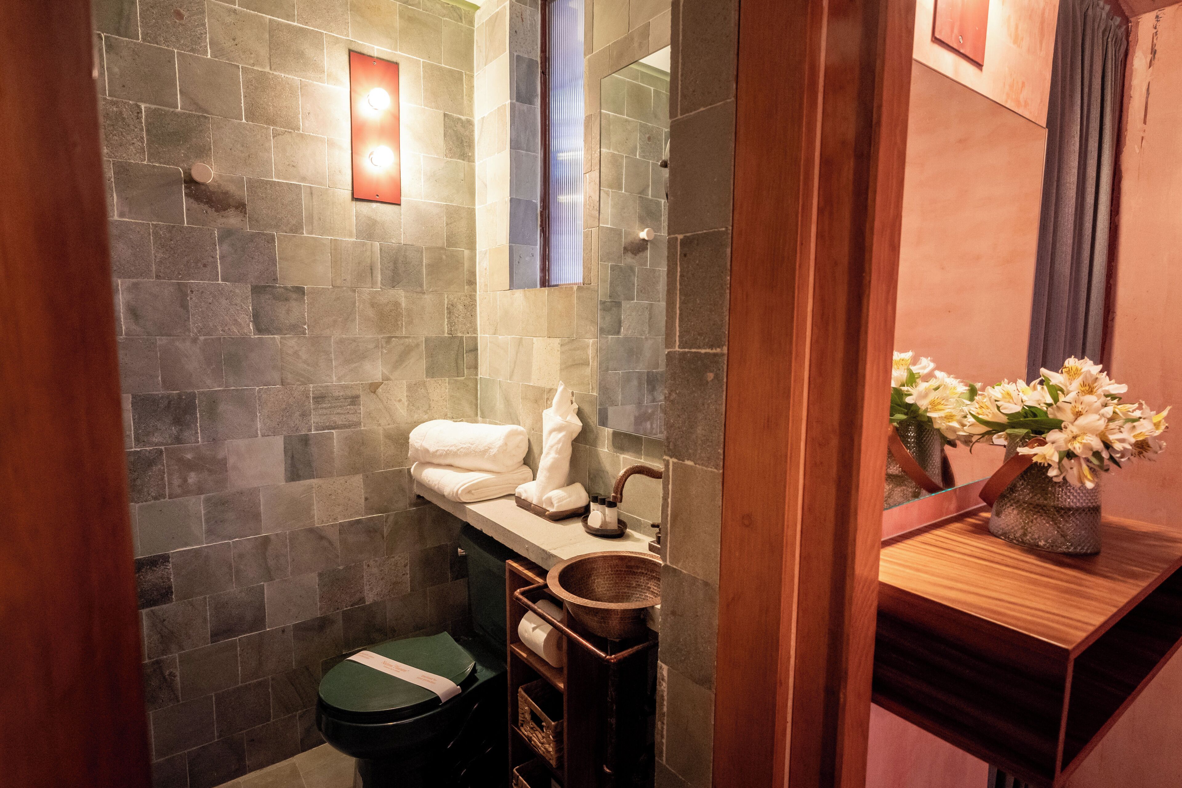 A bathroom with a stone wall, a wooden vanity, a sink, and a toilet.