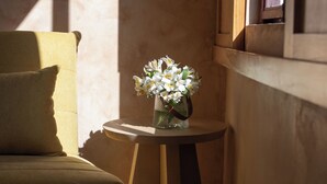 A corner of a room with a chair, a small table with a vase of flowers, and a window with sunlight casting shadows. - Hotel Casa de las Abuelas (Guanajuato)