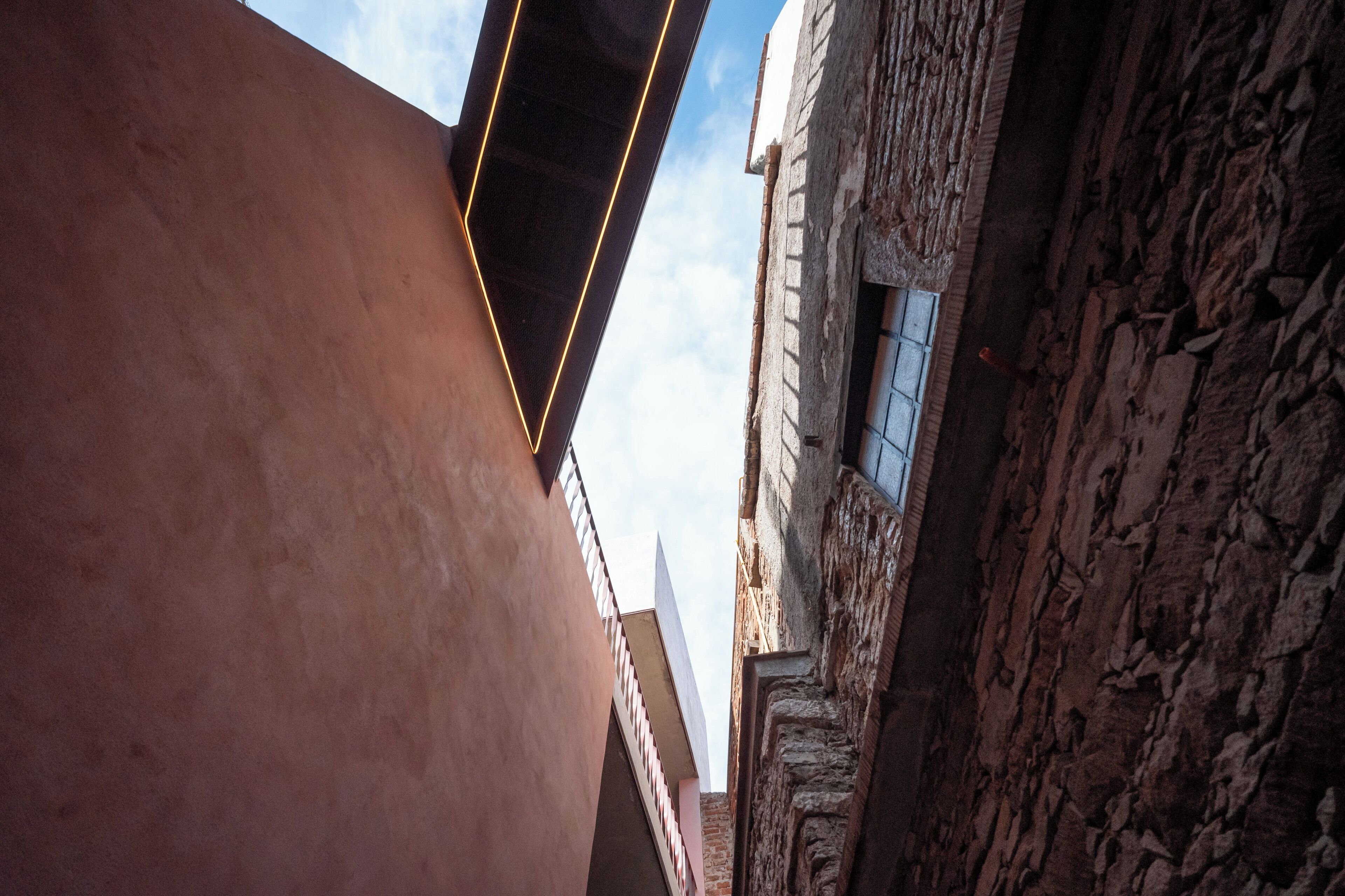 A narrow street with a stone building on the right and a modern building on the left.