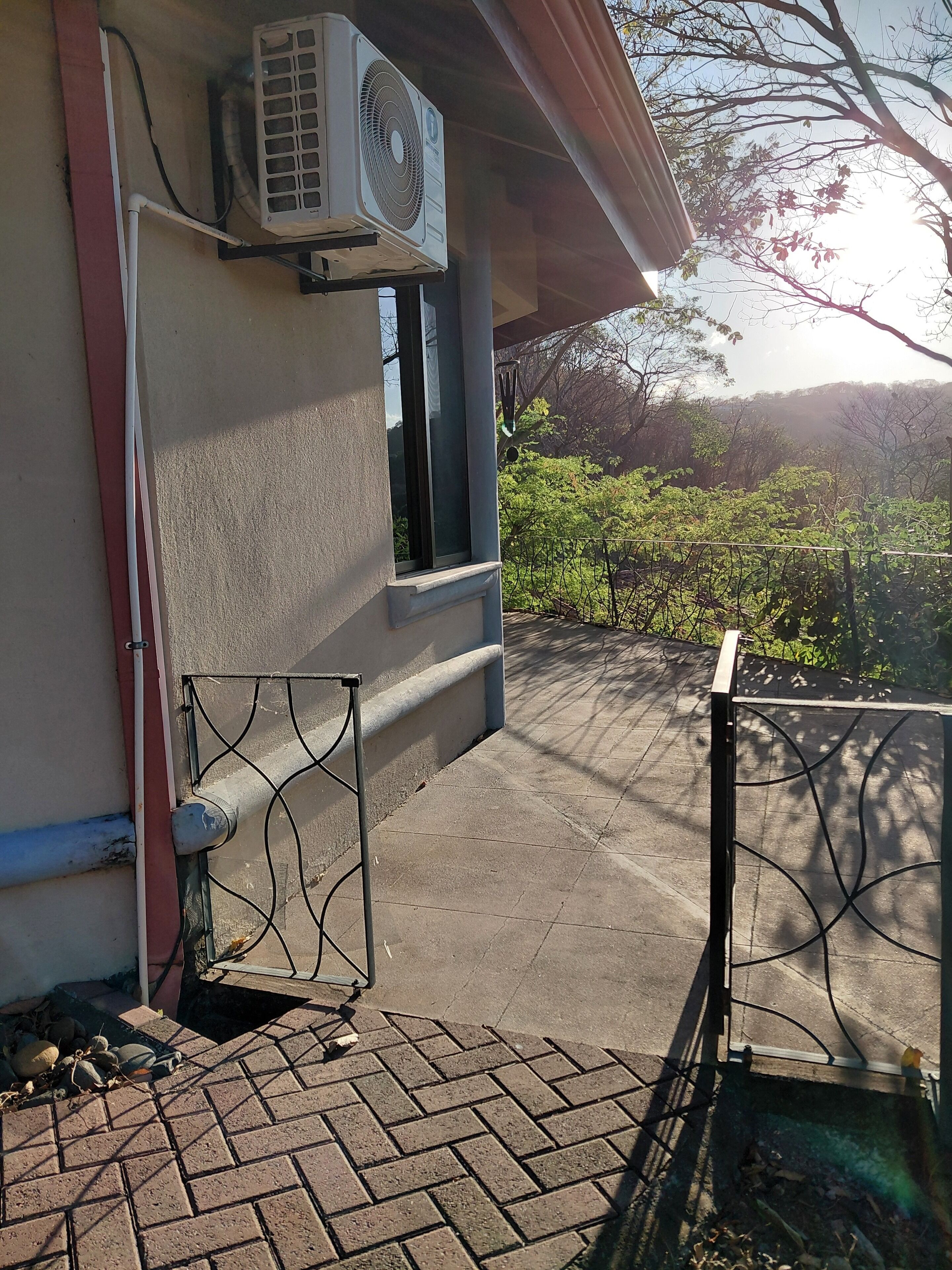 An outdoor area with a brick floor, a metal gate, and an air conditioning unit mounted on a wall.
