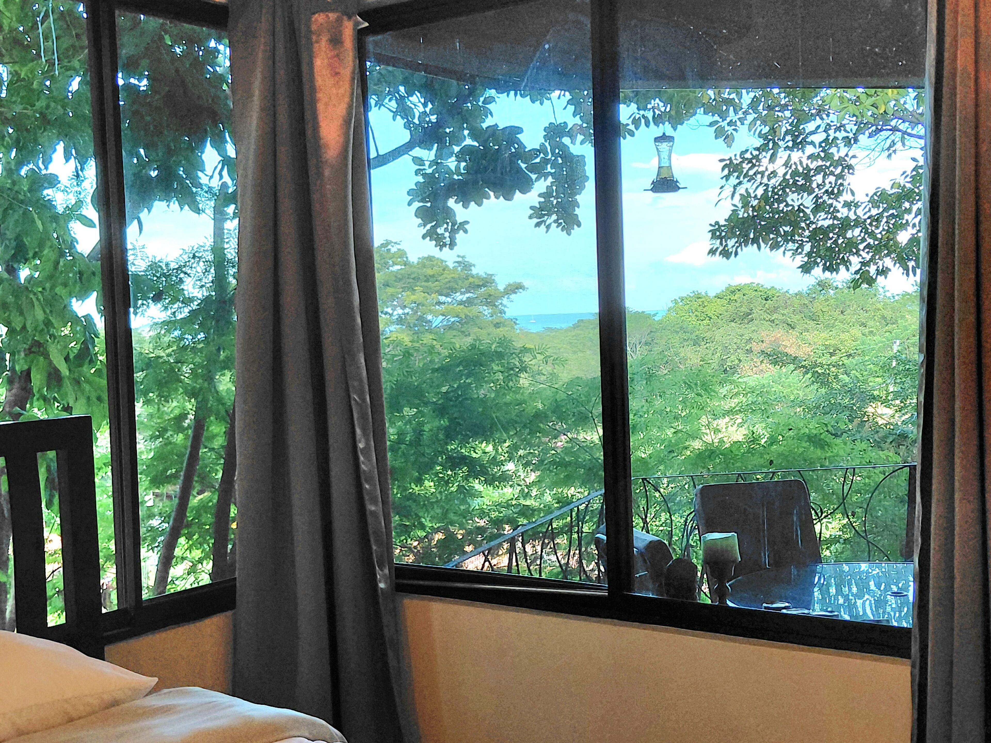 A room with a large window overlooking a lush green landscape and a view of the sea.