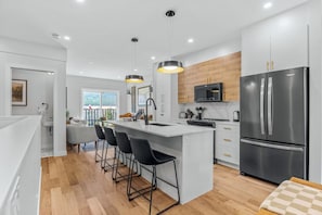 Een moderne keuken met een centraal eiland, barkrukken, roestvrijstalen apparatuur en hanglampen.