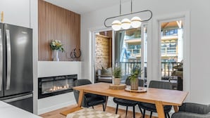 A modern kitchen with a built-in refrigerator, a fireplace, and a dining area with a wooden table and chairs. - 4BR Getaway with MTN View, Balcony Near DT & Banff! (Canmore)