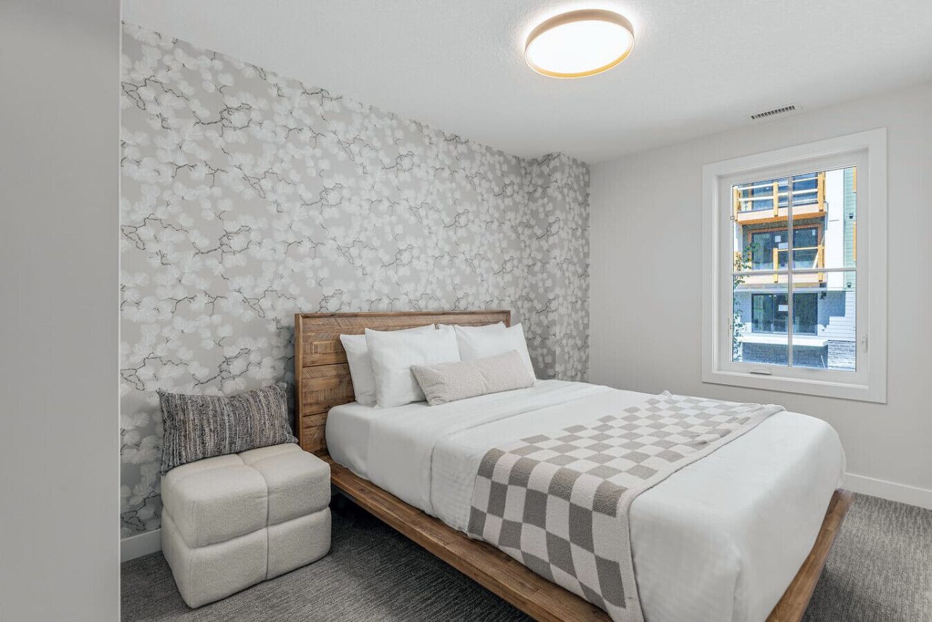Une chambre à coucher avec un lit en bois, une petite table de chevet et une fenêtre donnant sur des immeubles.