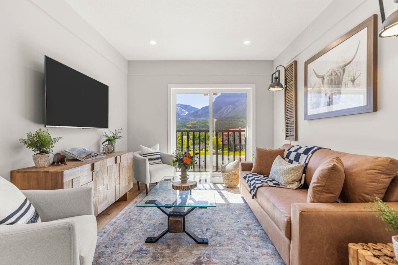 Un salon moderne comprenant un canapé, un fauteuil et une table basse, un téléviseur à écran plat et un balcon offrant une vue sur les montagnes.