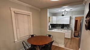 A dining area with a round wooden table and black chairs, a ceiling light fixture, and a kitchen in the background. - Cozy Home Near Ferndale, Royal Oak & Detroit! (Hazel Park)