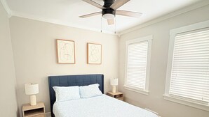 A bedroom with a bed, two bedside tables, a ceiling fan, and two framed artworks on the wall. - Cozy Home Near Ferndale, Royal Oak & Detroit! (Hazel Park)