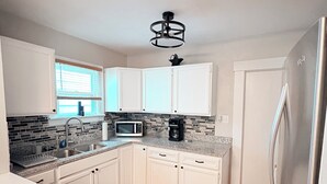 A modern kitchen with white cabinets, a stainless steel refrigerator, a microwave, and a coffee maker on the countertop. - Cozy Home Near Ferndale, Royal Oak & Detroit! (Hazel Park)