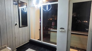 A modern interior with a large sliding glass door leading to a balcony, a ceiling-mounted smoke detector, and a minimalist design with a marble floor and a patterned rug. - BLACKSTORM RESIDENCY HOTEL (Greater Noida)