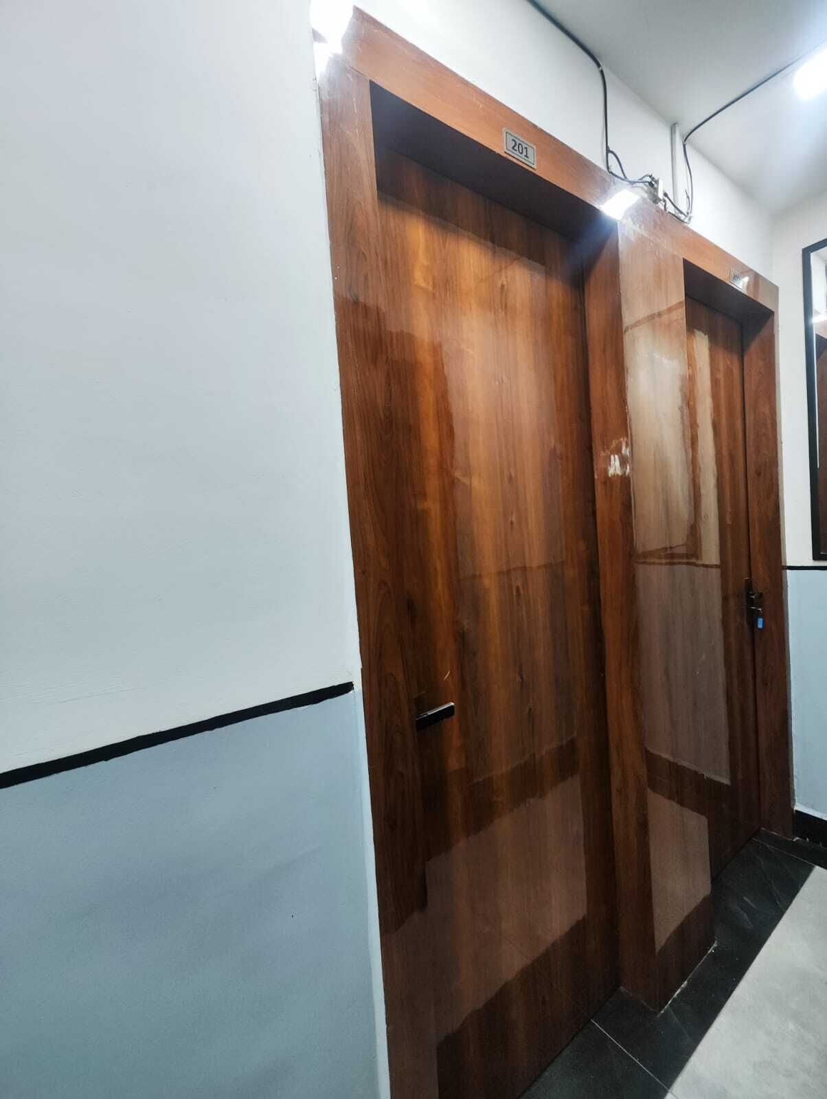 A wooden door with a number plate, a light fixture above it, and a tiled floor.