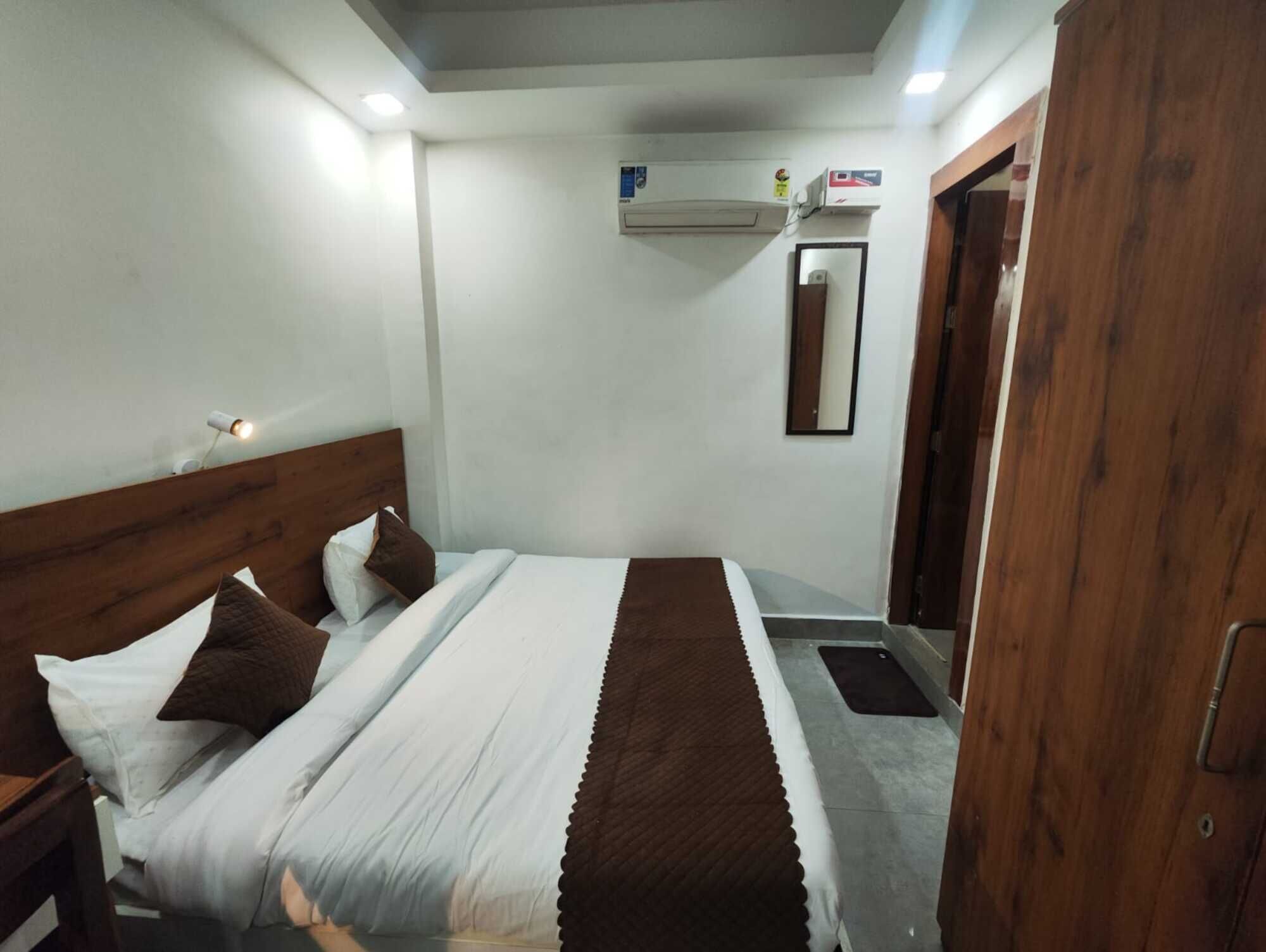 A hotel room with a bed, a nightstand, a mirror, an air conditioning unit, and a wooden door.