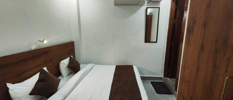 A hotel room with a bed, a nightstand, a mirror, an air conditioning unit, and a wooden door.