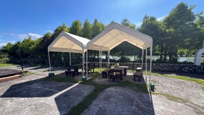 Two outdoor canopies with picnic tables and benches, set against a backdrop of trees and a body of water. - dream castle (Wujie)