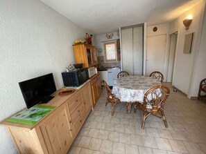 Una cocina compacta con comedor, armarios de madera, microondas, refrigerador pequeño y una mesa con sillas.
