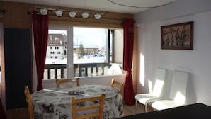 A dining area with a table and chairs, a window with curtains, and a painting on the wall. - Apartment in France Near Ski Lifts (Huez)