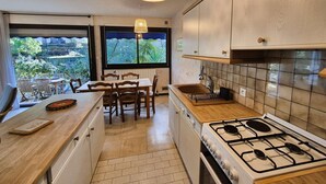 A modern kitchen with a gas stove, wooden cabinets, and a dining area with a view of the outdoors. - 2 rooms, WIFI, sea view, garden, private parking (ST MANDRIER SUR MER)