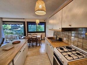 A modern kitchen with a gas stove, wooden cabinets, and a dining area with a view of the outdoors. - 2 rooms, WIFI, sea view, garden, private parking (ST MANDRIER SUR MER)