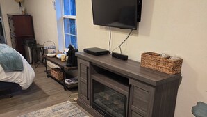 Una sala de estar con un televisor de pantalla plana montado en la pared, un mueble de centro de entretenimiento en madera oscura, un tapete grande y una ventana con cortinas azules.