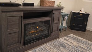Una sala de estar con un mueble de centro de entretenimiento de madera oscura, un televisor de pantalla plana montado encima y una chimenea con puerta de cristal.