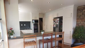 A modern kitchen with white cabinets, a central island with bar stools, a built-in oven, and a refrigerator with magnets. - Tasman Tranquility Cozy family home (Motueka)